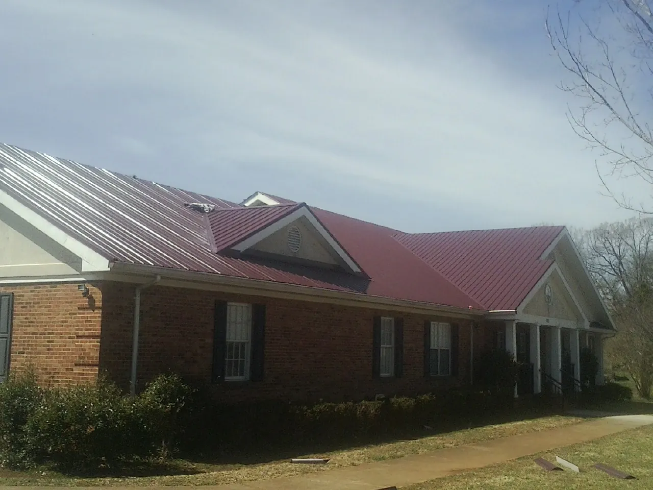 Red metal roof with gabled entries on a long brick building, from a Hail Damage Roof Repair job in Wood River Junction