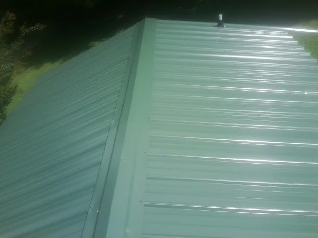 New green metal panels meeting at the ridge of a roof — Flat Roof Repair work by our crew in Wood River Junction