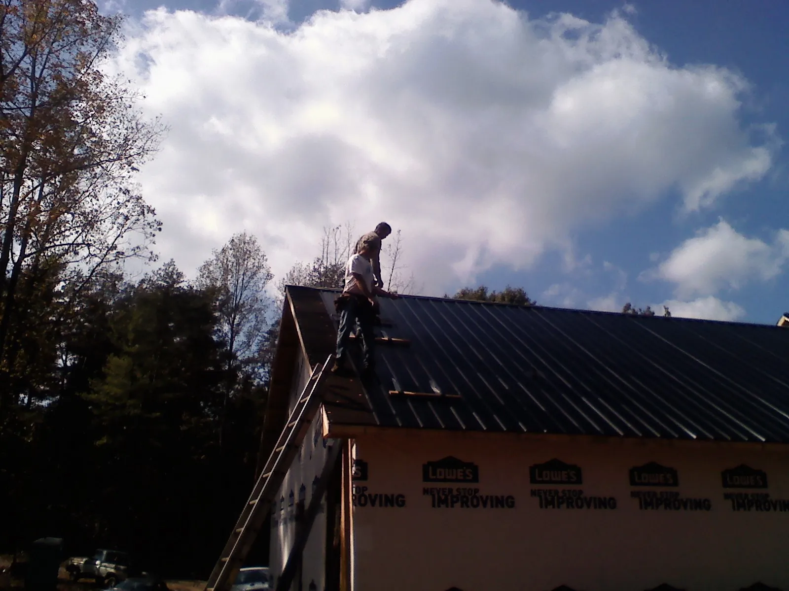 Roofer fastening dark metal panels high against a cloudy sky, from a Roof Inspection job in Wood River Junction
