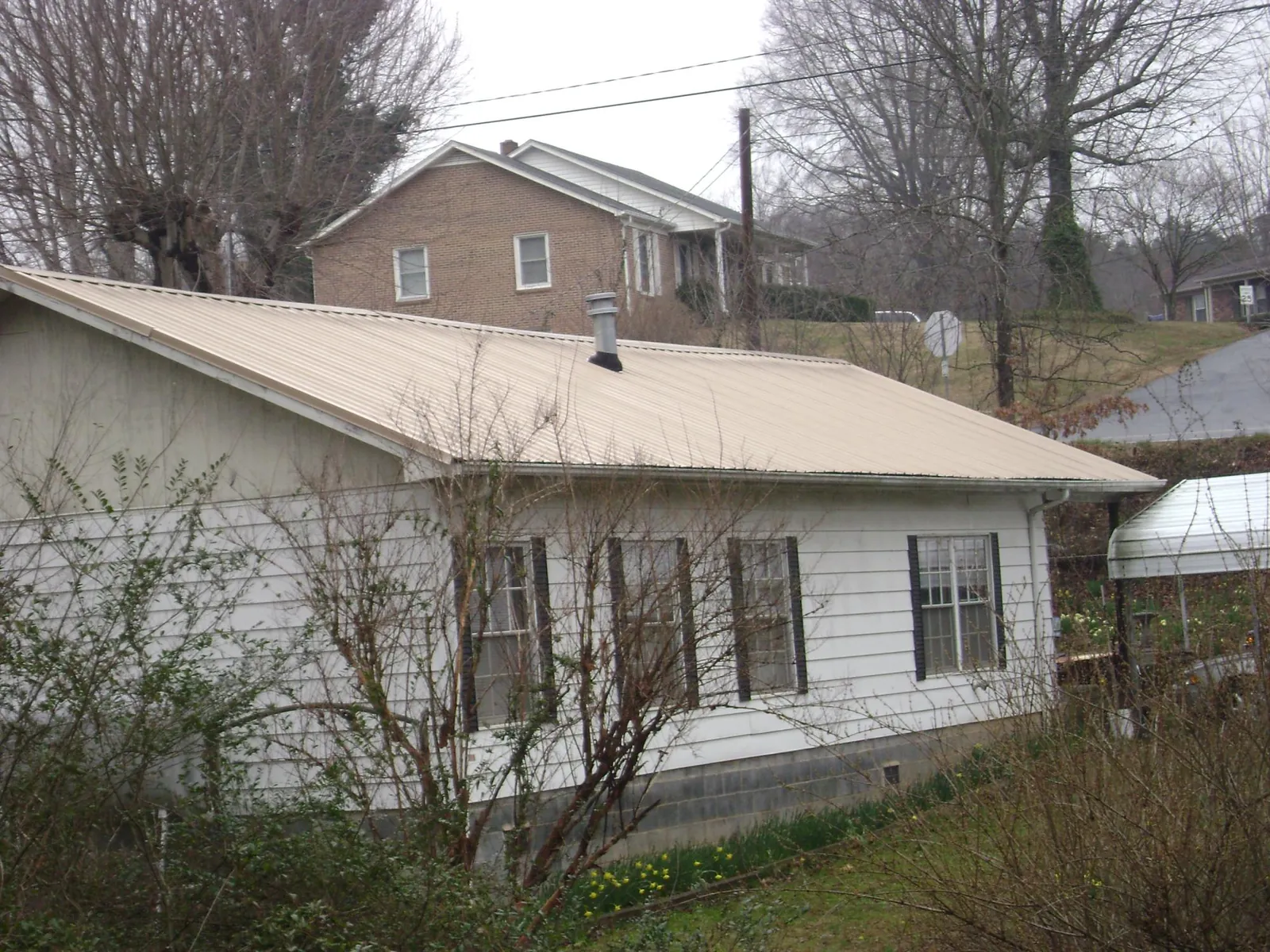 Tan metal roof on a white sided house set into a hillside — Commercial Roofing by Roofing Brothers in Wood River Junction